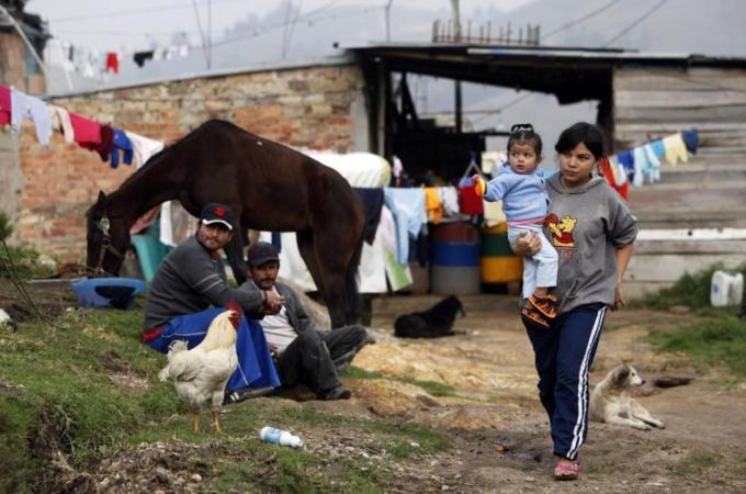 An internally displaced woman carrying a child walks by two men sitting on the ground in the Altos de la Florida neigbourhood of Bogota