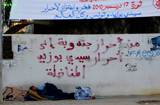 The graffiti above the man sleeping on the street in Sidi Bouzid reads 'From the free of Jenduba to the free of the fighting Sidi Bouzid' [Mohamed M'dalla/Al Jazeera]