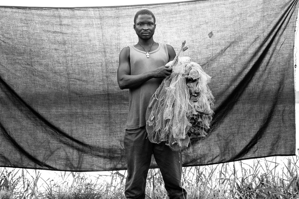 Jean Gerembo recalls Wednesday March 27, 2013, vividly. His wife and two children were staying with his mother-in-law, when Seleka forces entered his village of Batalimo. The Seleka heard from a neighbour that Jean(***)s mother had saved some money, and at 11:45 that night there came a knock at the door. Jean hid beneath his mother(***)s bed and told her to remain silent, and not to answer it. A few moments later, the door was kicked in. One of the soldiers walked over to the bed and slit the old woman(***)s throat. Terrified, Jean stayed under the bed as they looted the home. The next morning, he found eight young people who were, as he said, "brave enough to to help me to bury my mother." After the burial, Jean found his family, gathered a few essentials, and together they fled across the Oubangi River in his small fishing boat. The most important thing that Jean was able to bring with him from CAR was his fishing net. He says that the net allows him to live, and to earn. "Some of the fish I sell, some we eat. I use the money to buy clothes and to pay the local people for plantains, cassava and peanuts," he said. "Many people have suffered. Mine is just one story." 