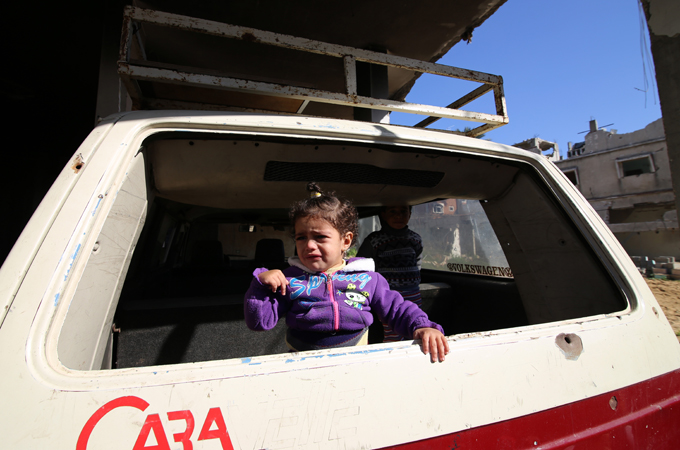 A young girl cries as she looks out at her destroyed neighbourhood [Hatem Omar/Al Jazeera]