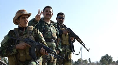 Kakai fighters monitor ISIL positions in the distance by a sign that reads the village of Kobane as Kurdistan flags are blown by the wind [Mohammed A Salih/Al Jazeera] 