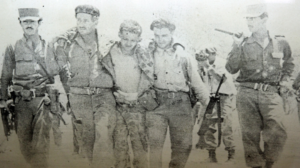 A photo of a photograph of captured Cubans exiles, with Julio Simoneau filming in the background [Robert Kennedy/Al Jazeera]
