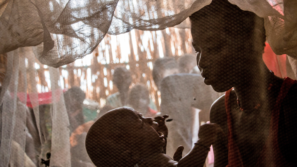 A young mother cradles her baby inside a hut that serves as a school in the Bentiu camp [Ashley Hamer/Al Jazeera]
