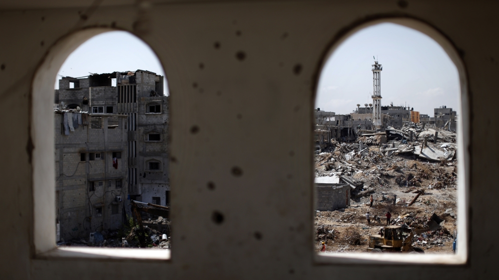 Seen through the windows of a damaged apartment, Palestinian workers clear the rubble of destroyed buildings in the eastern Gaza City neighborhood of Shejaiya which was heavily targeted during the 50-