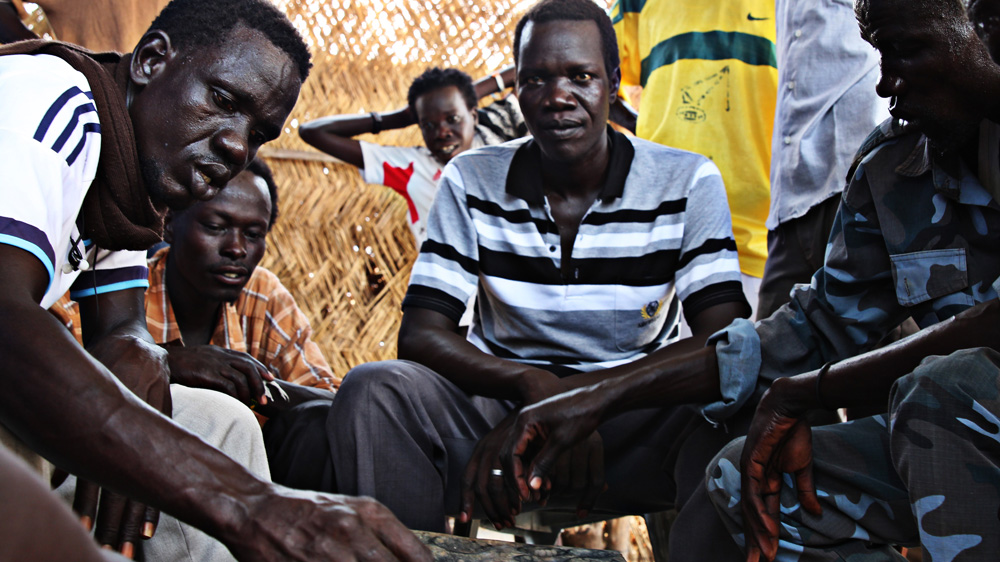 Men, some in police uniform, play a game in Wau Shilluk near one of the tents that houses Olony's soldiers [Simona Foltyn/Al Jazeera]