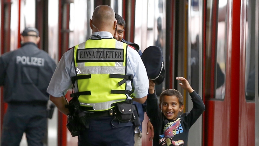 A refugee boy tries on a security officer's cap after arriving in Germany [Reuters]