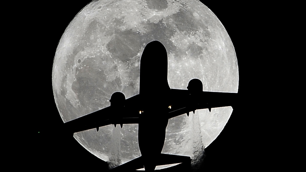 A passenger plane en route to Los Angeles International Airport passes in front of a full moon [AP]