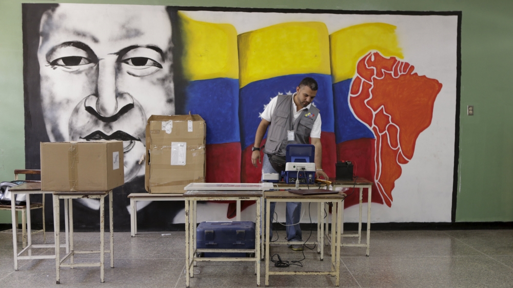A worker of the National Electoral Council (CNE) configures a voting machine in front of a mural depicting Venezuela''s late President Hugo Chavez at a school in Caracas