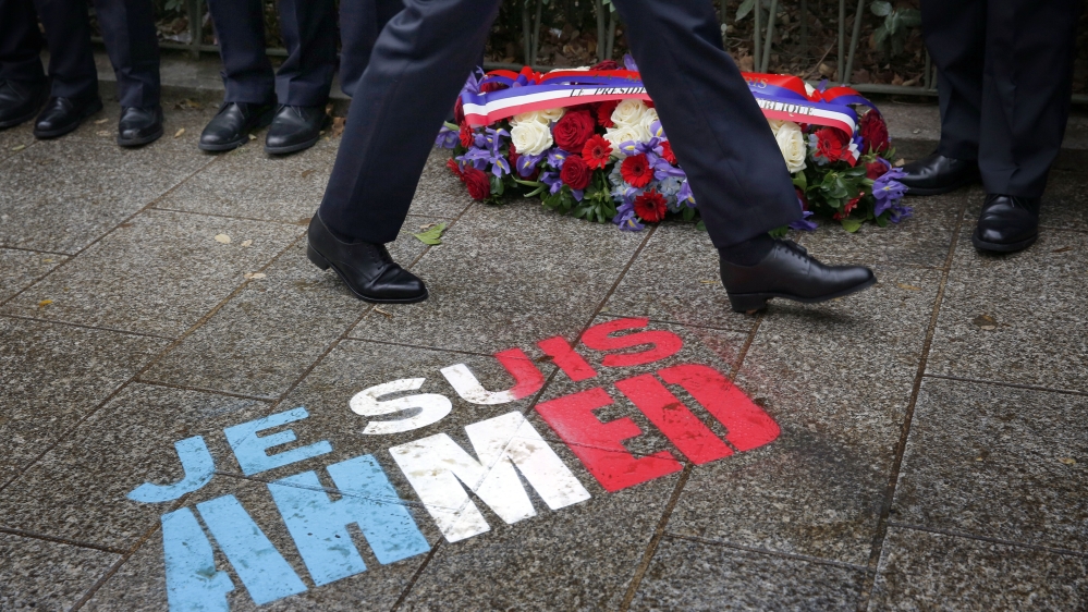 Policemen walk past spray painted on the sidewalk reading: "Je suis Ahmed," in the red, white and blue of the French flag near a plaque commemorating late police officer Ahmed Merabet in Paris [AP]