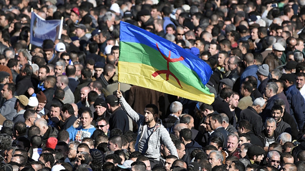 A man waves the Amazigh flag as thousands of mourners attend the funeral procession and burial of one of the fathers of Algeria''s struggle for independence [AFP]