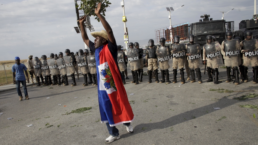 A protester holding a branch reacts in front of a police cordon during a protest against the electoral process in Port-au-Prince, Haiti