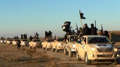 ISIL fighters hold up their weapons and wave its flags in a convoy on a road leading to Iraq, in Raqqa, Syria [AP]