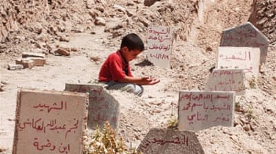 An Iraqi boy prays over graves in a makeshift cemetery on a soccer field in Fallujah, Iraq [Getty]