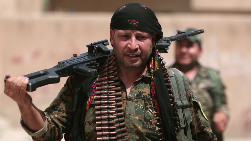 A Kurdish fighter from the People''s Protection Units (YPG) carries his weapons as he walks along a street in the northeastern city of Hasaka
