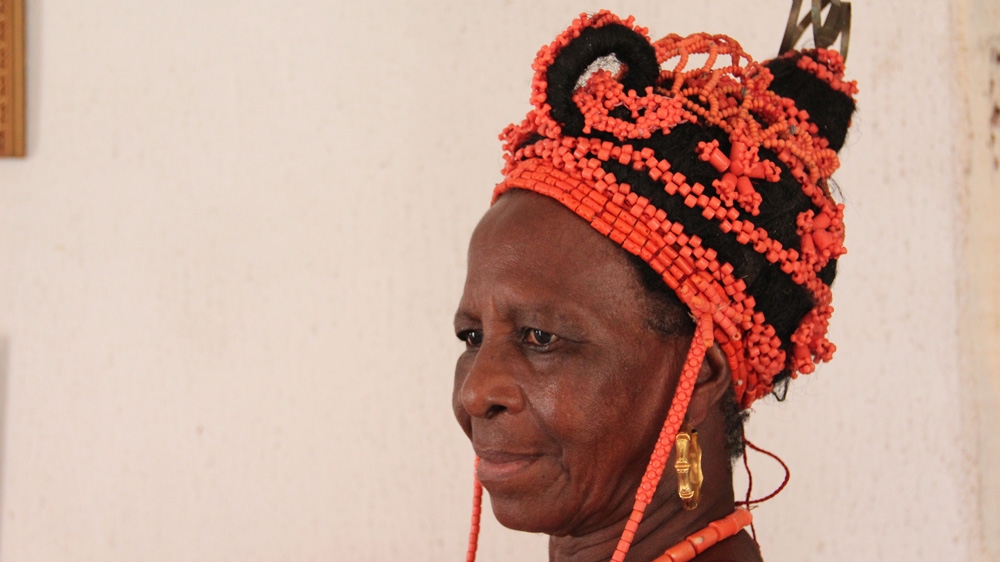 Princess Elizabeth Olowu, sister of the late king and aunt of the new one, tries on the headgear she'll wear at the coronation [Femke van Zeijil/Al Jazeera] 