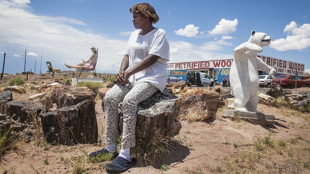 Gazell Stewart sits in her garden of oddities that include a concrete polar bear, dinosaurs, mannequins, and trunks of petrified trees outside her shop, Stewart's Petrified Wood [Gabriela Campos/Al Jazeera]