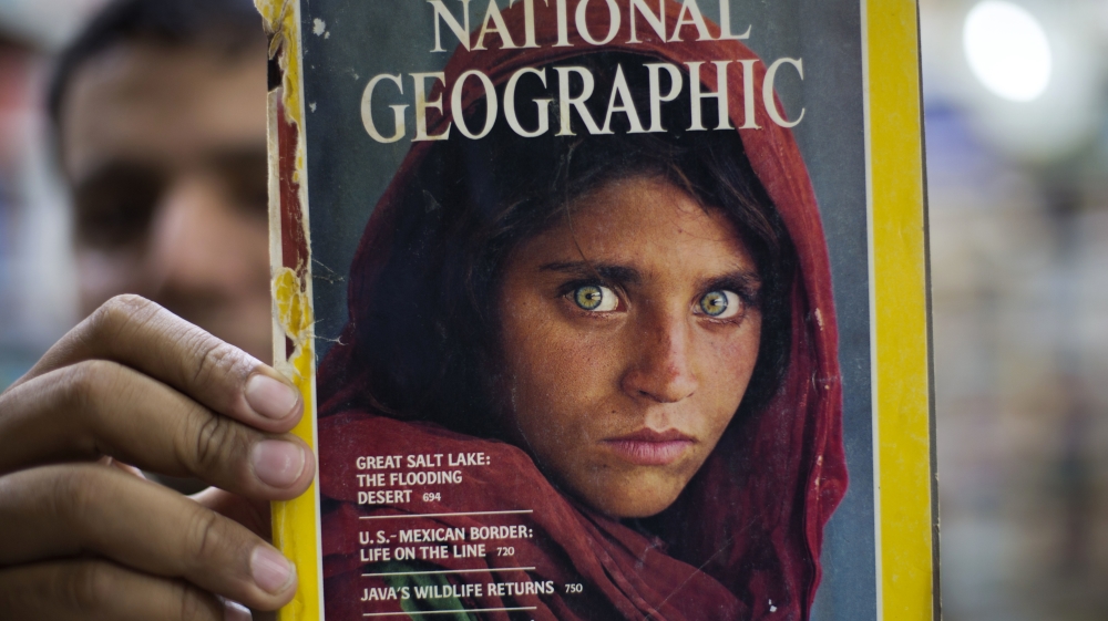 An owner of a bookshop shows a copy of a magazine with the famous photograph of Afghan refugee Sharbat Gula [BK Bangash/AP]