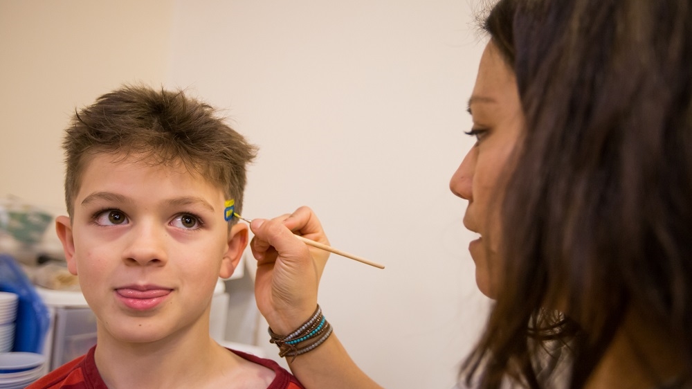 Natalia paints an equality sign on the head of Boden, Myles' brother and Natalia's other charge [Carolyn Bick/Al Jazeera]