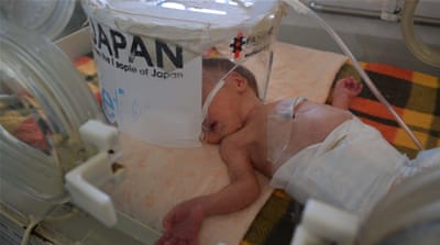 A baby lies underneath a broken oxygen hood held together by masking tape [Mersiha Gadzo/Al Jazeera]