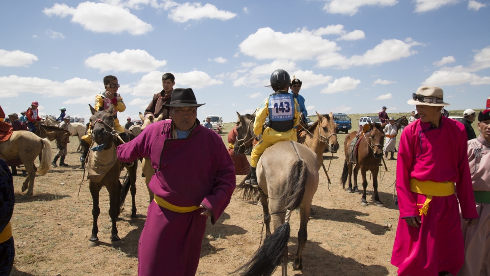 Bujinlkham, dressed in yellow, awaits the start of the 24km race atop one of her family’s horses at the Naadam festival in Tsagaandelger [Hannah Griffin/Al Jazeera]