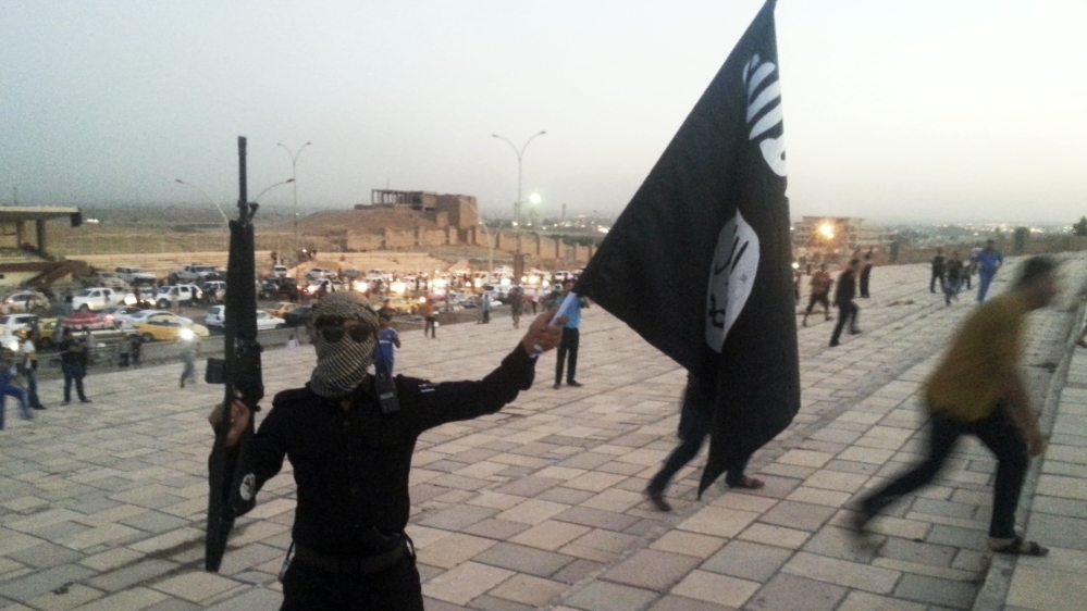 A fighter of the ISIL holds a flag and a weapon on a street in Mosul