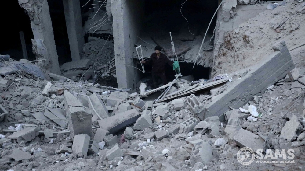 A man walks out of a building's rubble carrying two crutches in Eastern Ghouta [Courtesy of SAMS]