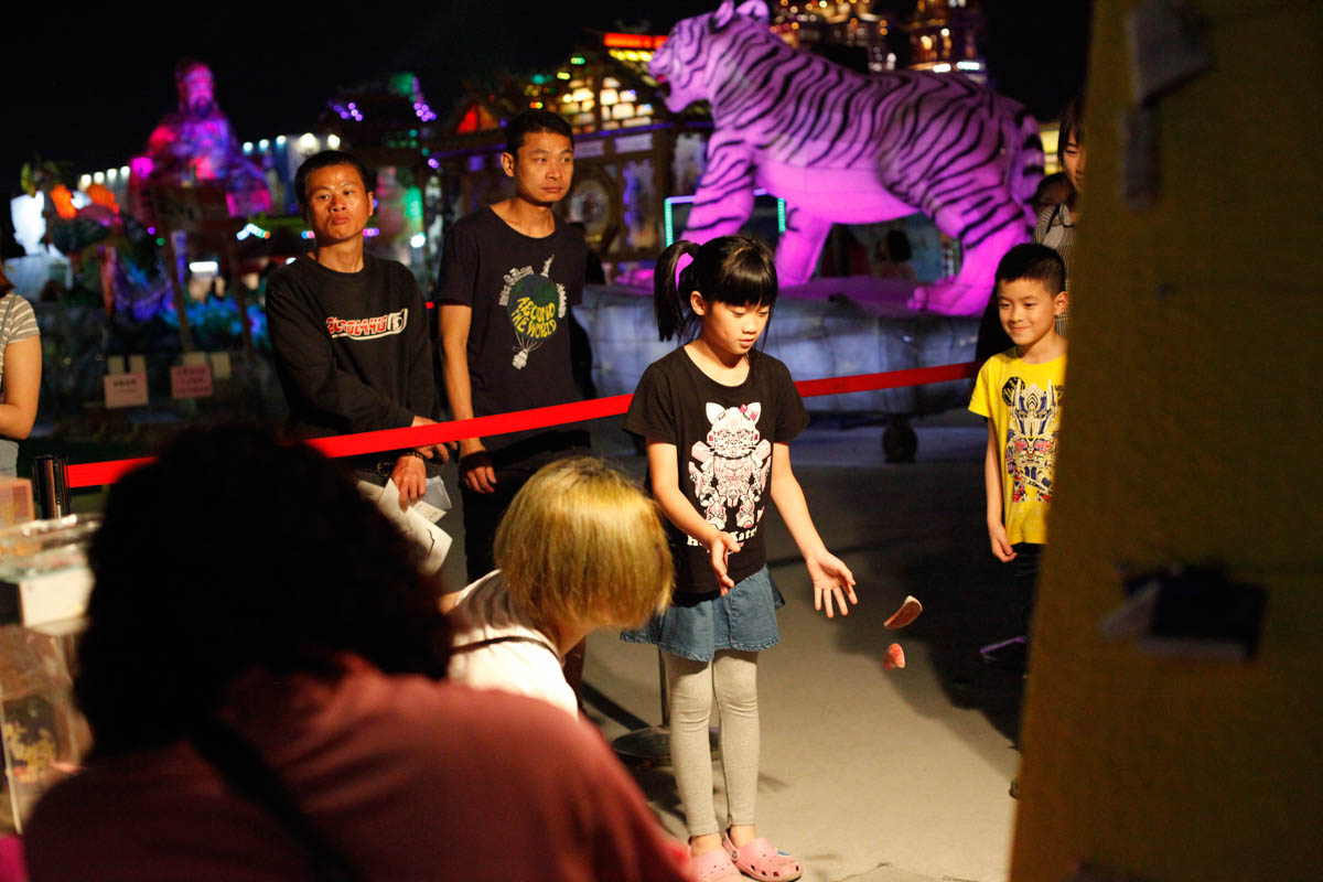 A girl casts traditional moon blocks on the floor, waiting to see if she gets good luck. In this small corner of Taiwan Lantern Festival, people stand in line and take chances to cast moon blocks. The