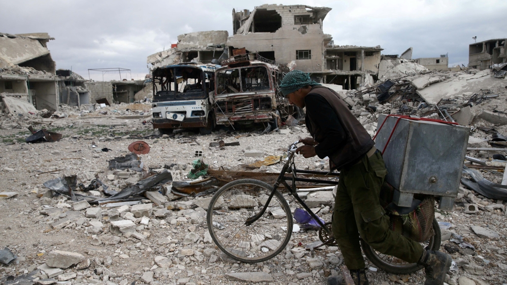 A man walks with his bicycle at a damaged site in the besieged town of Douma