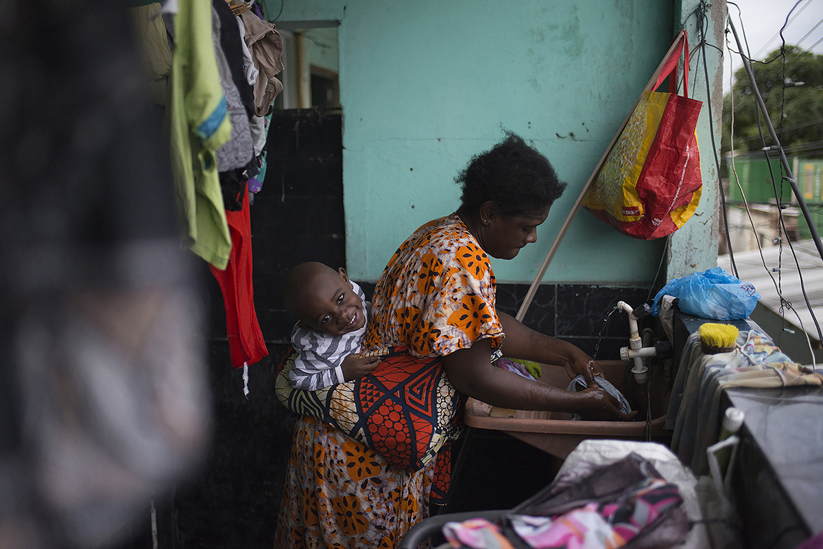 A single mother from the Democratic Republic of Congo, washes clothes with her son in the Bras de Pina favela where she lives in northern Rio. She works at a beauty parlor, styling the hair of African