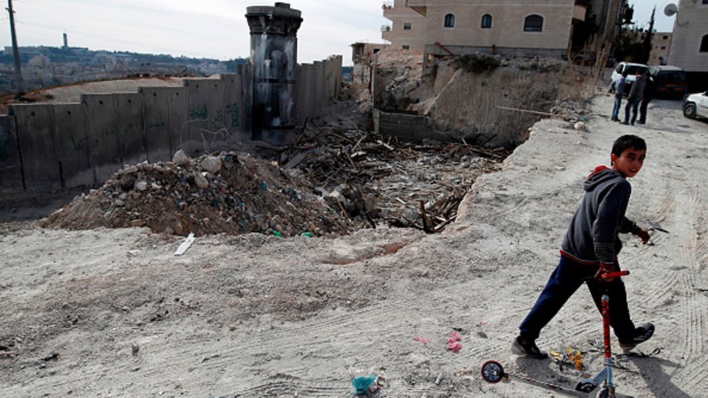 A Palestinian boy walks with his scooter past the rubble of an illegally-built house, which was demolished by Jerusalem municipality workers, in the refugee camp of Shuafat