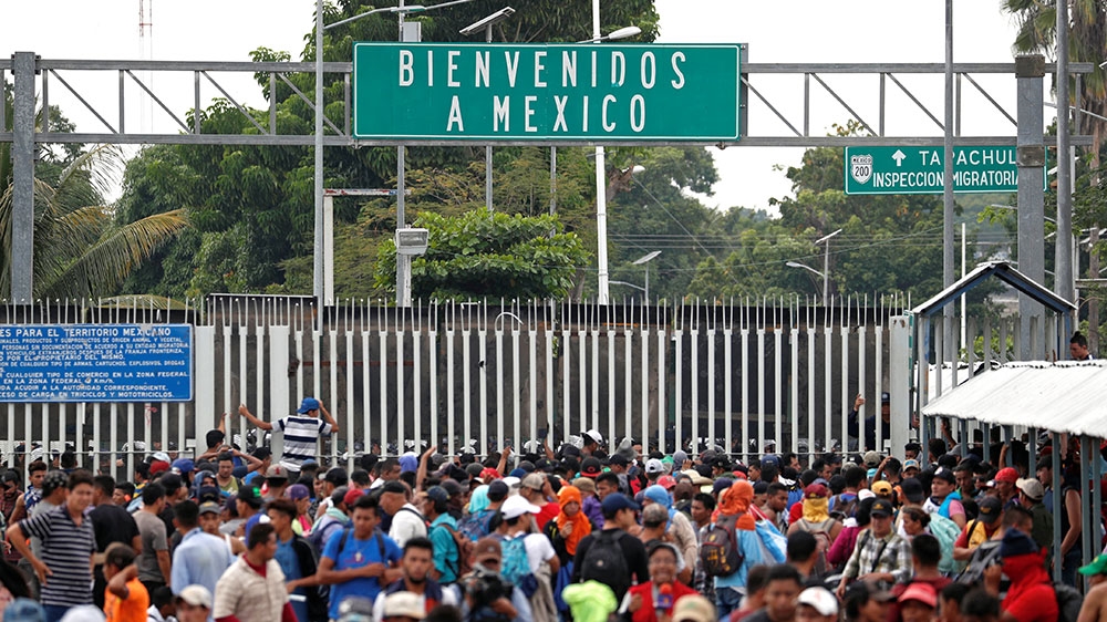 Central Americans, part of a caravan trying to reach the US, stand near the Mexican border gate on the bridge between Guatemala and Mexico as they try to cross into Mexico [Carlos Garcia Rawlins/Reuters] 