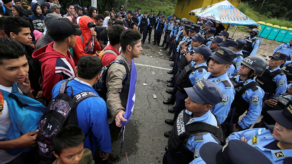 Honduras immigrants stand in front of Honduran police officers blocking the access to the Agua Caliente border with Guatemala as they try to join a migrant caravan heading to the US [Jorge Cabrera/Reuters] 