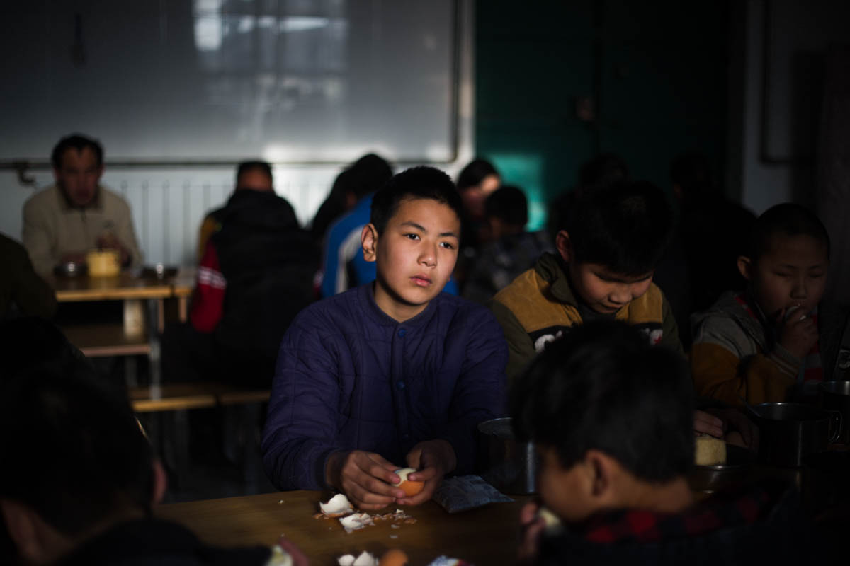 A student shares lunch with his friends. Life at the school is communal and the students share dormitories and social spaces.