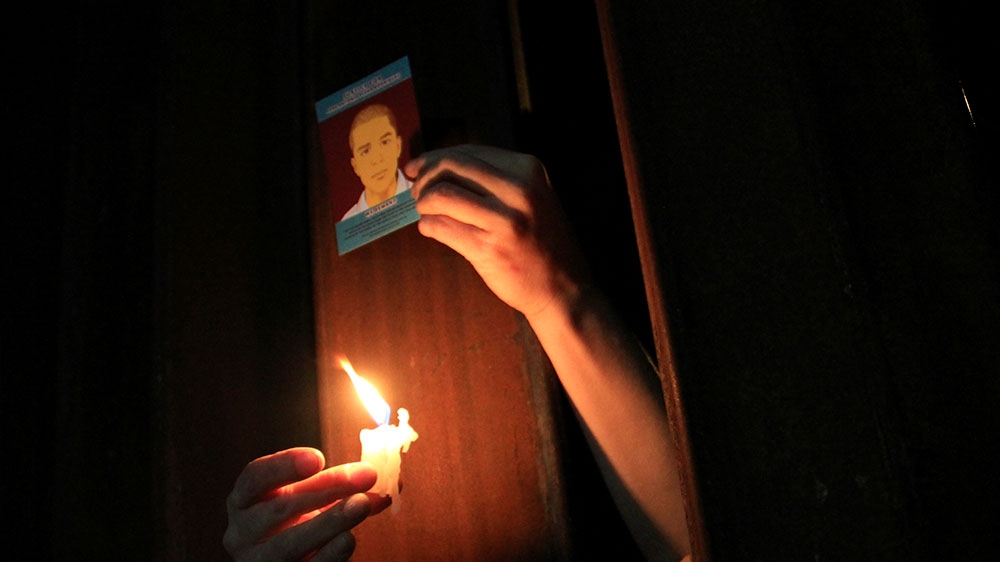 A US pro-migration activist holds a candle and a picture of slain Mexican youth Jose Antonio Elena Rodriguez through the border fence between Mexico and the US in Nogales [File: Alonso Castillo/Reuters]