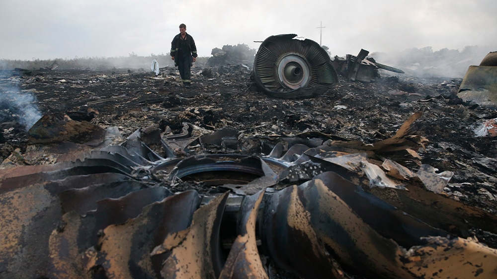 The blackened remains of an aircraft engine and other debris from MH17 in a field in eastern Ukraine. A man is standing in the background