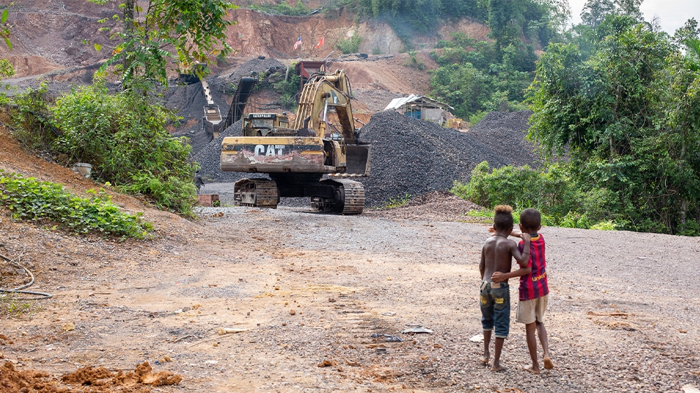 Two young Batek boys watch an excavator at the mine next to the village of Kuala Koh
