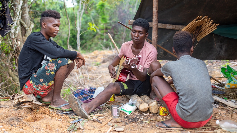 Batek villagers play the guitar next to their shelter in Kuala Koh