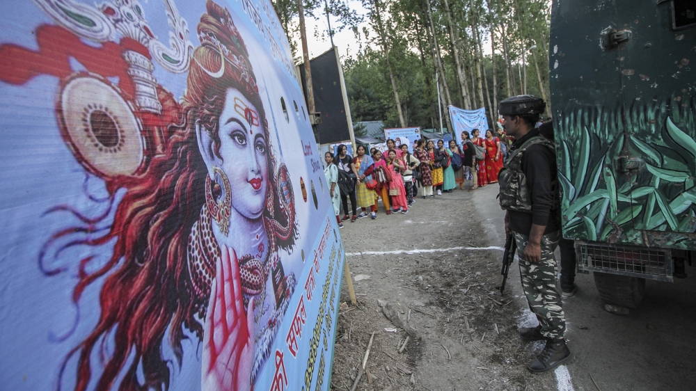 An Indian soldier stands next to a poster of Hindu god Lord Shiva as pilgrims march to the Amarnath cave