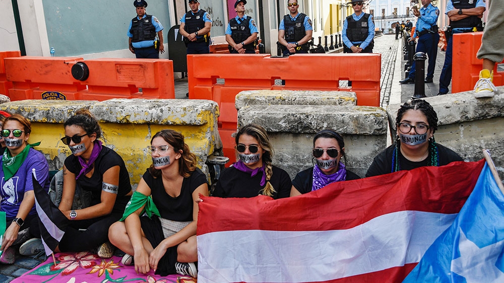 A group of women tape their mouths with tape that reads ‘Resign’ during the fourth day of protest calling for the resignation of Governor Ricardo Rossello in San Juan