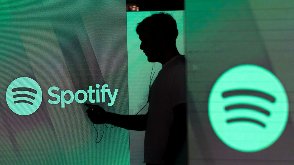 A man checks his smartphone whilst standing amongst illuminated screens bearing the Spotify Technology