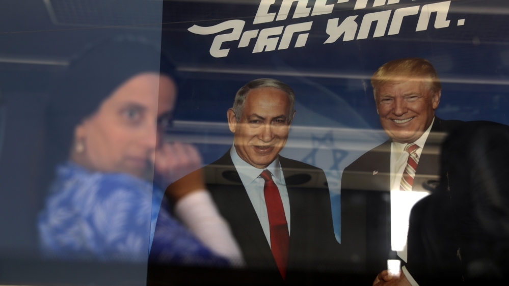 An ultra-orthodox Jewish woman is seen through a bus window along with a reflection of a Likud party election campaign banner depicting Israeli Prime Minister Benjamin Netanyahu and Trump