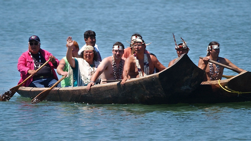 Wiyot Tribe tribal chair Cheryl Seidner waves as she travels by dugout redwood canoe from Indian Island across Humboldt Bay to a deed ceremony in Eureka, California