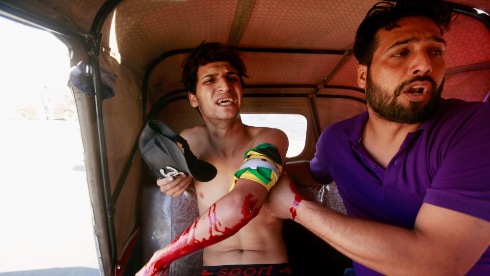 A man is seen assisting an injured demonstrator at a protest during a curfew, three days after the nationwide anti-government protests turned violent, in Baghdad