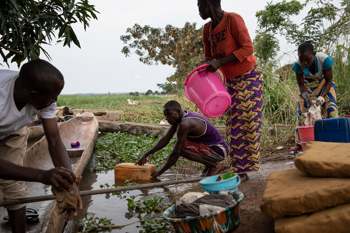 Grâce à Dieu, the son of Île aux Singe’s chief, is cleaning a boat next to people taking the Ubangi River’s water to wash clothes and utensils. Twice a day, they receive a bucket of drinkable water. N