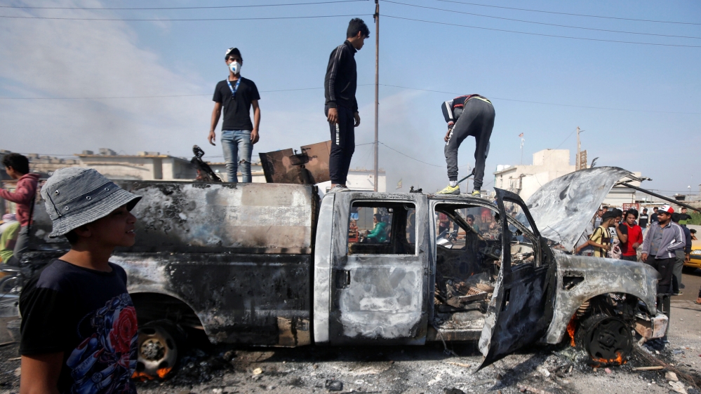 Protesters step on a military vehicle of Iraqi security forces after burning it, during ongoing anti-government protests in Basra