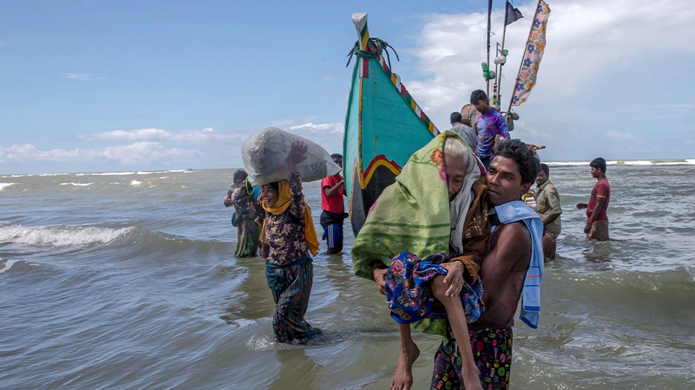 A Rohingya Muslim man walks to shore carrying an elderly woman after they arrived on a boat from Myanmar to Bangladesh in Shah Porir Dwip, Bangladesh, nearly three weeks after fleeing violence in Myanmar, September 14, 2017 [Dar Yasin/AP]