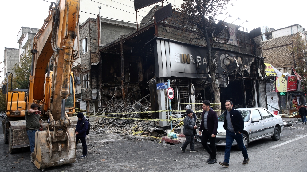 People walk near a burnt bank, after protests against increased fuel prices, in Tehran