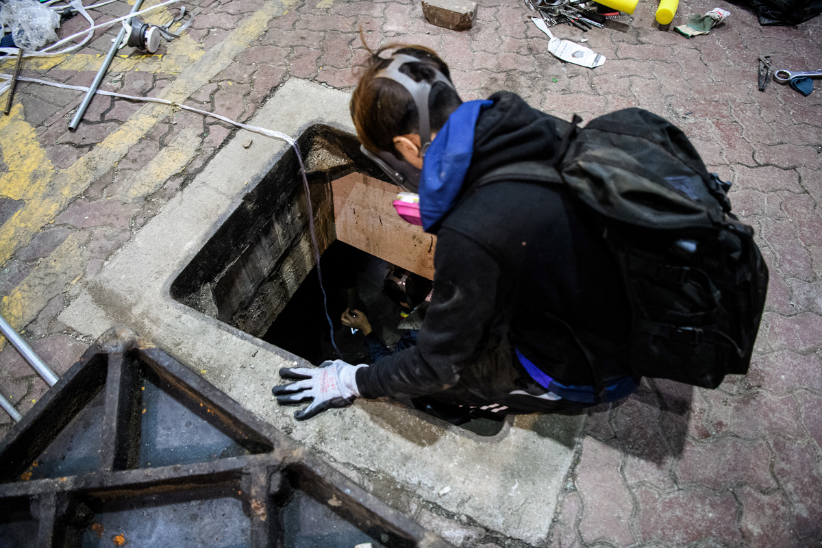 A protester climbs down into a sewer entrance as he and others try to find an escape route from the Hong Kong Polytechnic University in the Hung Hom district of Hong Kong, early morning on November 19