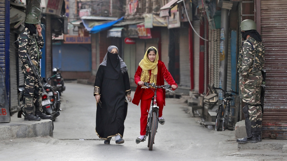 A Kashmir girl rides her bike past Indian security force personnel standing guard in front closed shops in a street in Srinagar, October 30, 2019. REUTERS/Danish Ismail TPX IMAGES OF THE DAY