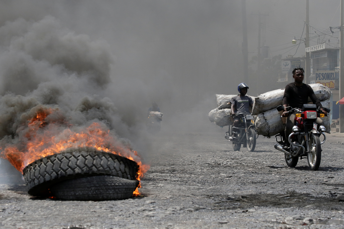 Men riding motorbikes pass next to a burning tire at a barricade in a street of Port-au-Prince, Haiti October 2, 2019. REUTERS/Andres Martinez Casares